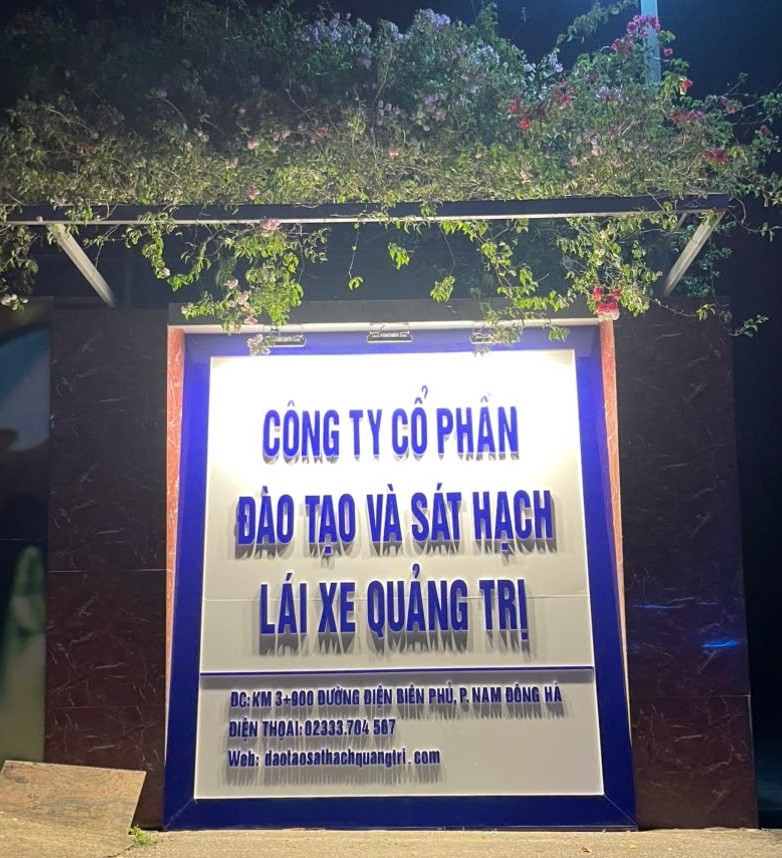 Ảnh biển hiệu "CÔNG TY CỔ PHẦN ĐÀO TẠO VÀ SÁT HẠCH LÁI XE QUẢNG TRỊ" ban đêm, có hoa giấy phía trên.